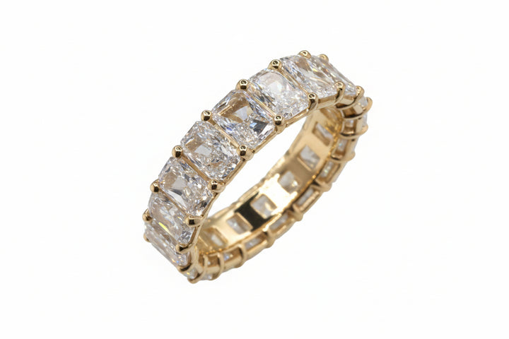 A yellow gold eternity ring featuring a row of rectangular clear gemstones, displayed on a white background.