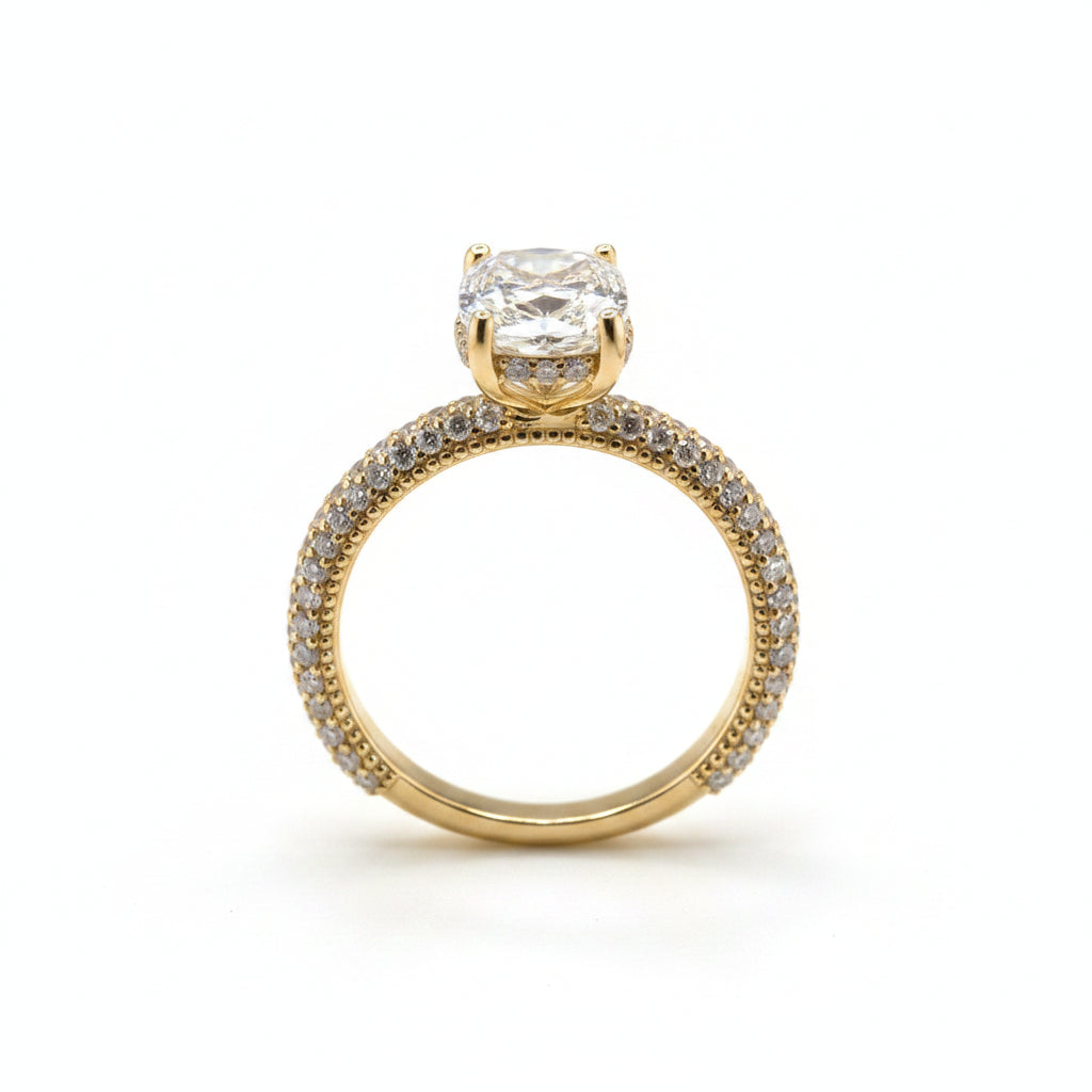 A yellow gold engagement ring with a cushion-cut diamond center stone and a pavé-set diamond band, displayed on a white background.
