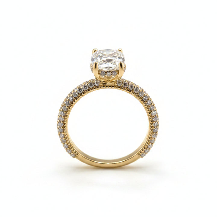 A yellow gold engagement ring with a cushion-cut diamond center stone and a pavé-set diamond band, displayed on a white background.